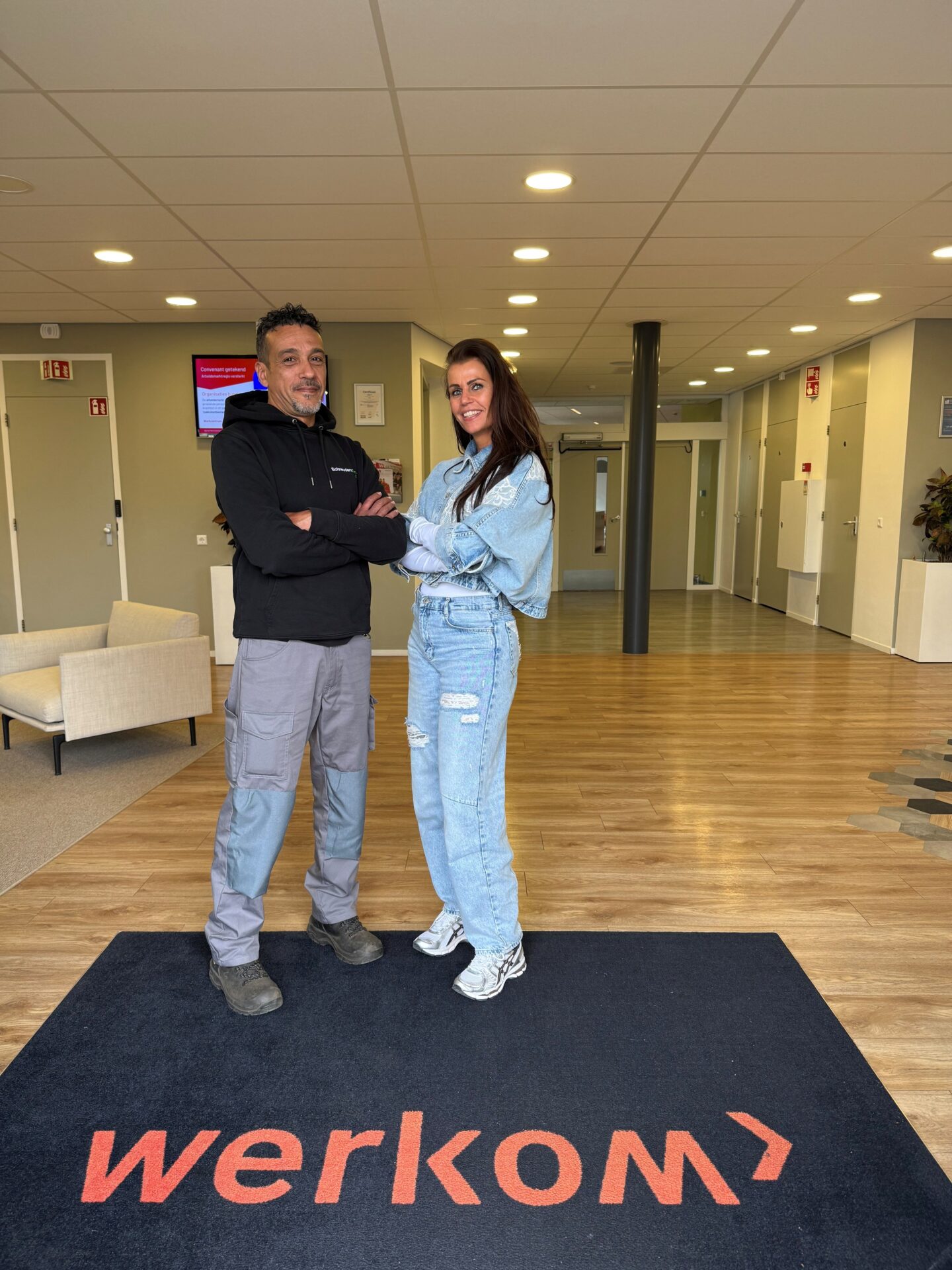 Foto van Andrea, man in zwarte hoodie, werkbroek en werkschoenen samen met Andrea, vrouw gekleed in spijkerbroek en jas